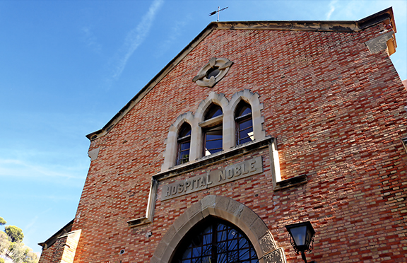 Fachada principal del antiguo edificio Hospital Noble de estilo neogótico construido en ladrillo visto con una ventana triple de arcos ojivales y una puerta de arco ojival